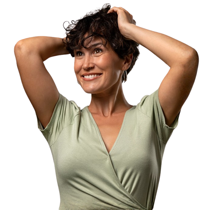 Smiling woman with short curly hair wearing a light green wrap dress holding her hands behind her head.