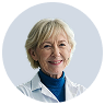 Smiling older woman with short blonde hair wearing a white coat and blue shirt.
