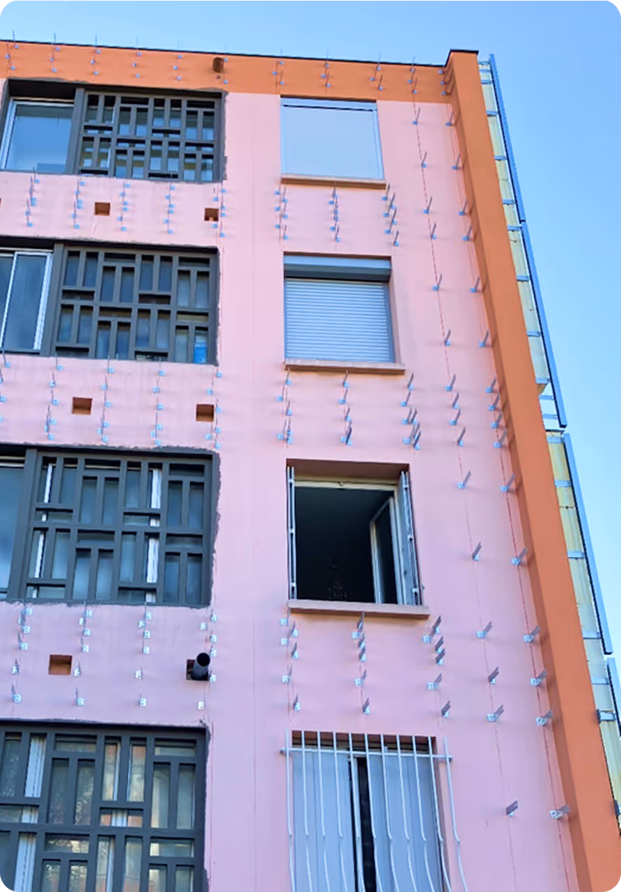 Façade rose d'un immeuble avec plusieurs fenêtres, accompagné dans le cadre d'une mission de rénovation énergétique par le bureau d'études RENER.