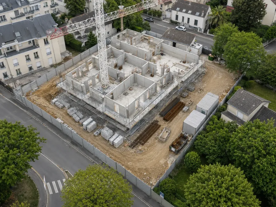 Aerial view of a construction site for a concrete building surrounded by houses and trees.