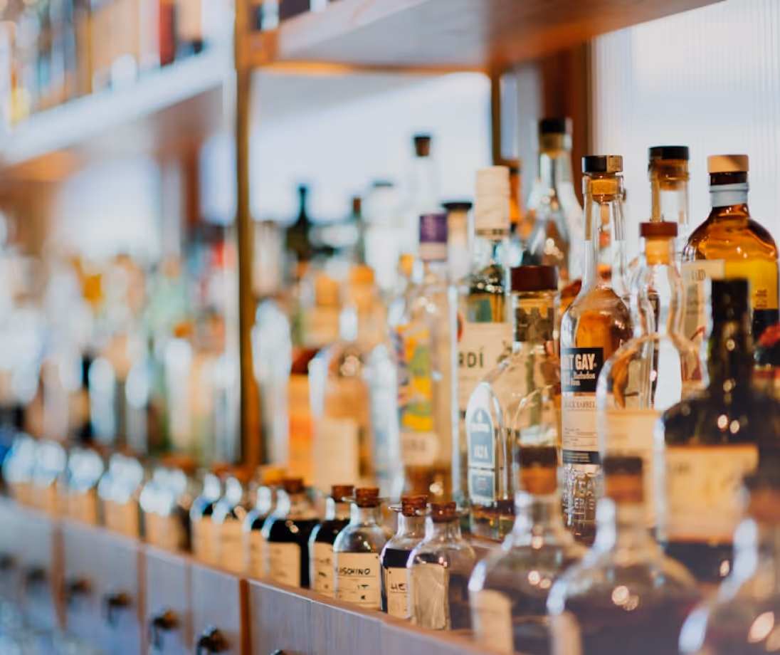 Shelf filled with various bottles of alcoholic beverages in a bar setting.