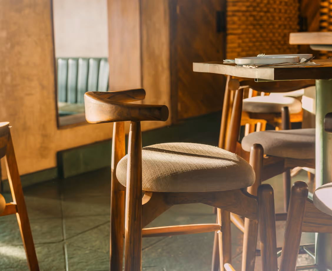 Wooden chair with beige cushion near a table set with plates in warm sunlight indoors.
