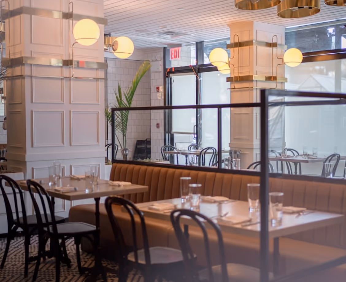 Elegant restaurant interior with tables, brown bench seating, black chairs, and round wall lights.