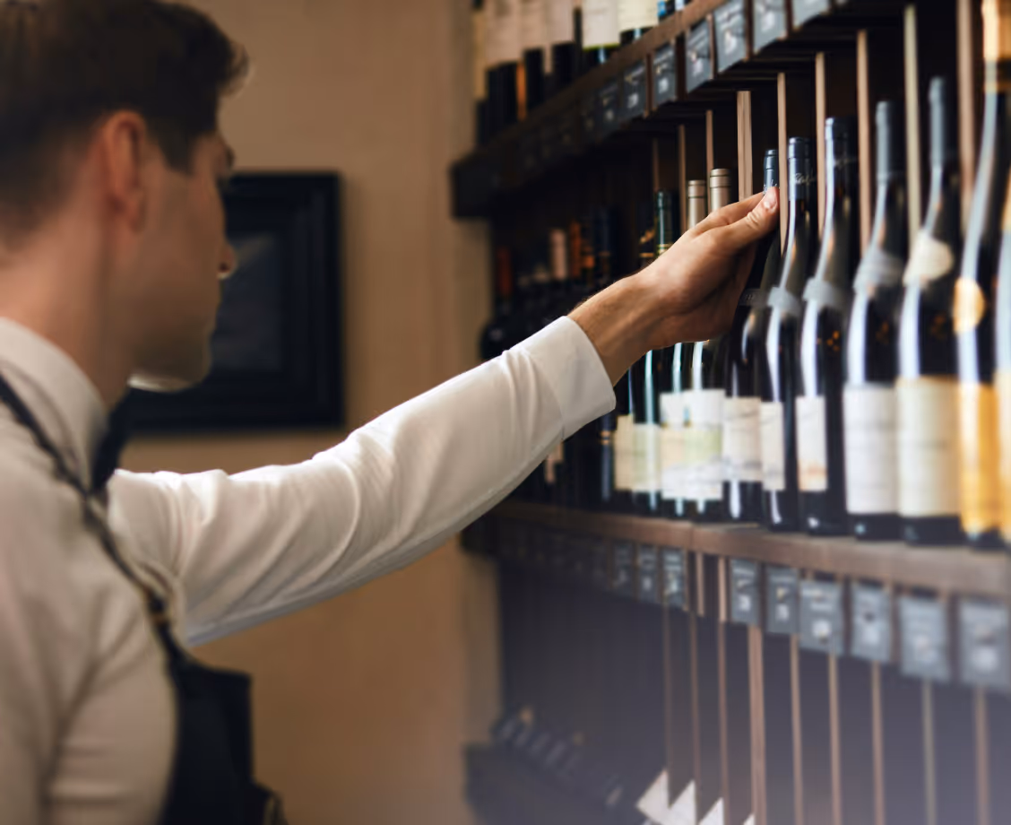 Person reaching for a wine bottle on a shelf filled with various liquor bottles.