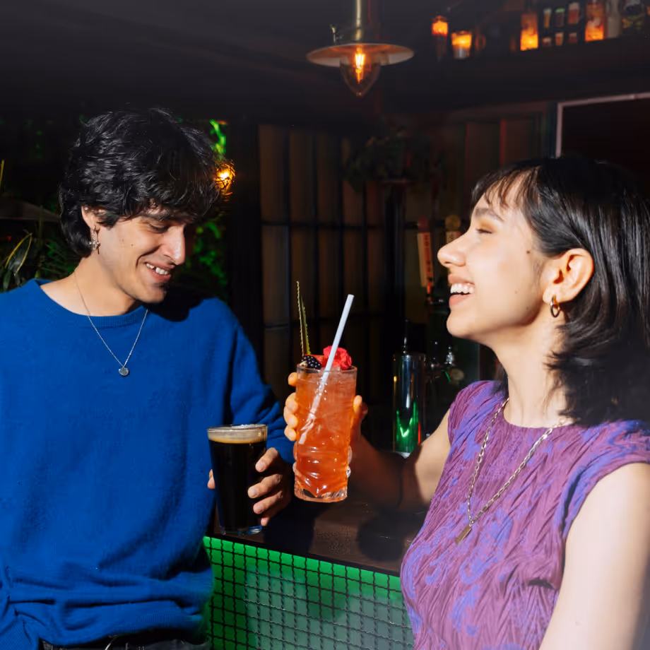 Two people enjoying drinks and smiling at a bar during happy hour.