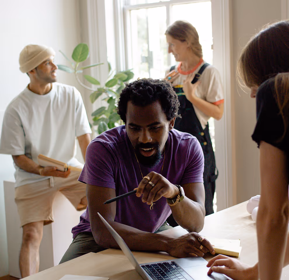 Group of four diverse people collaborating around a table with a laptop in a bright room.