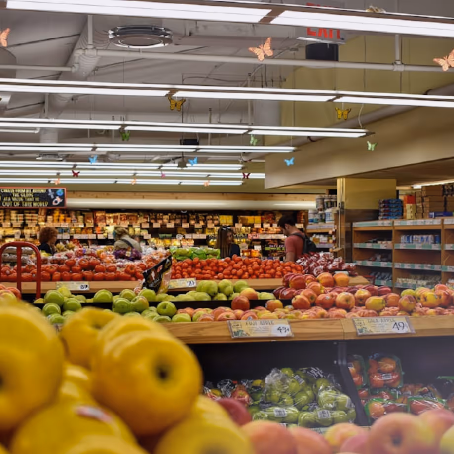 Customers shop for fresh fruits like apples and tomatoes in a grocery store produce section.