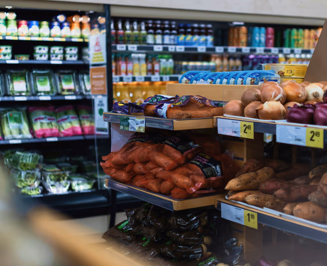 Grocery store shelves with onions, sweet potatoes, bagged carrots, and assorted packaged goods in the background.