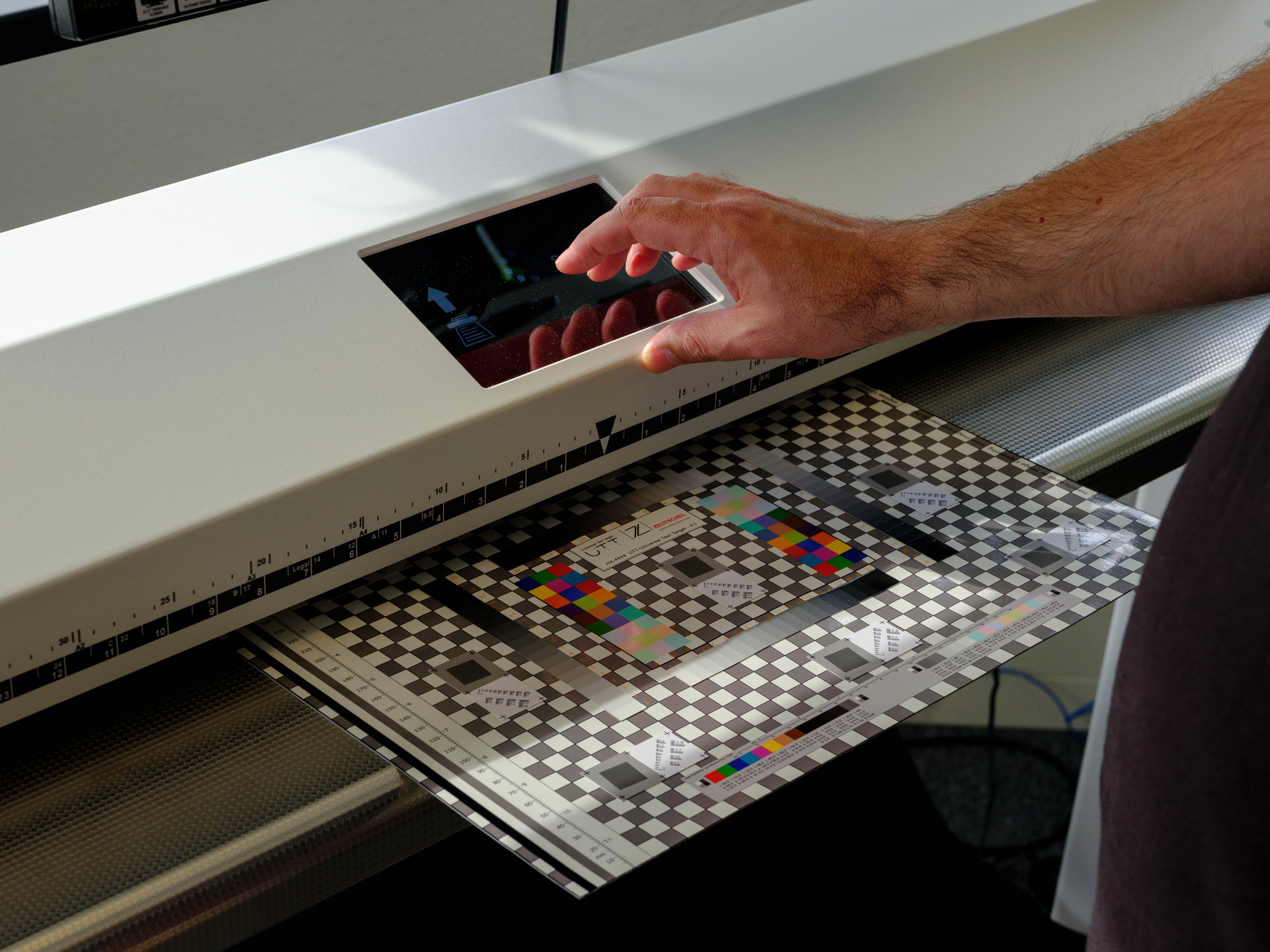Technician feeding a colour calibration target into a large-format scanner