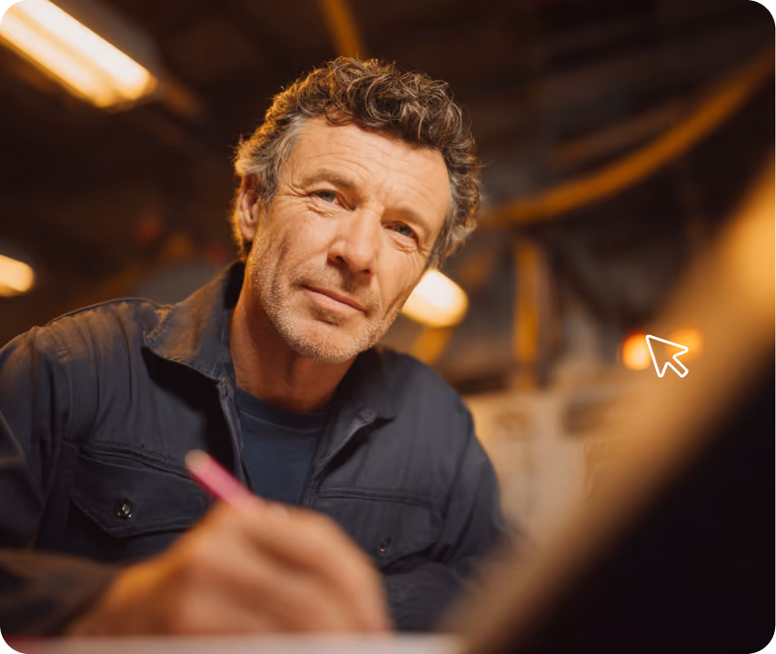 Mann mit grauen Haaren und Bart, der in einer Werkstatt mit Stift in der Hand schreibt.