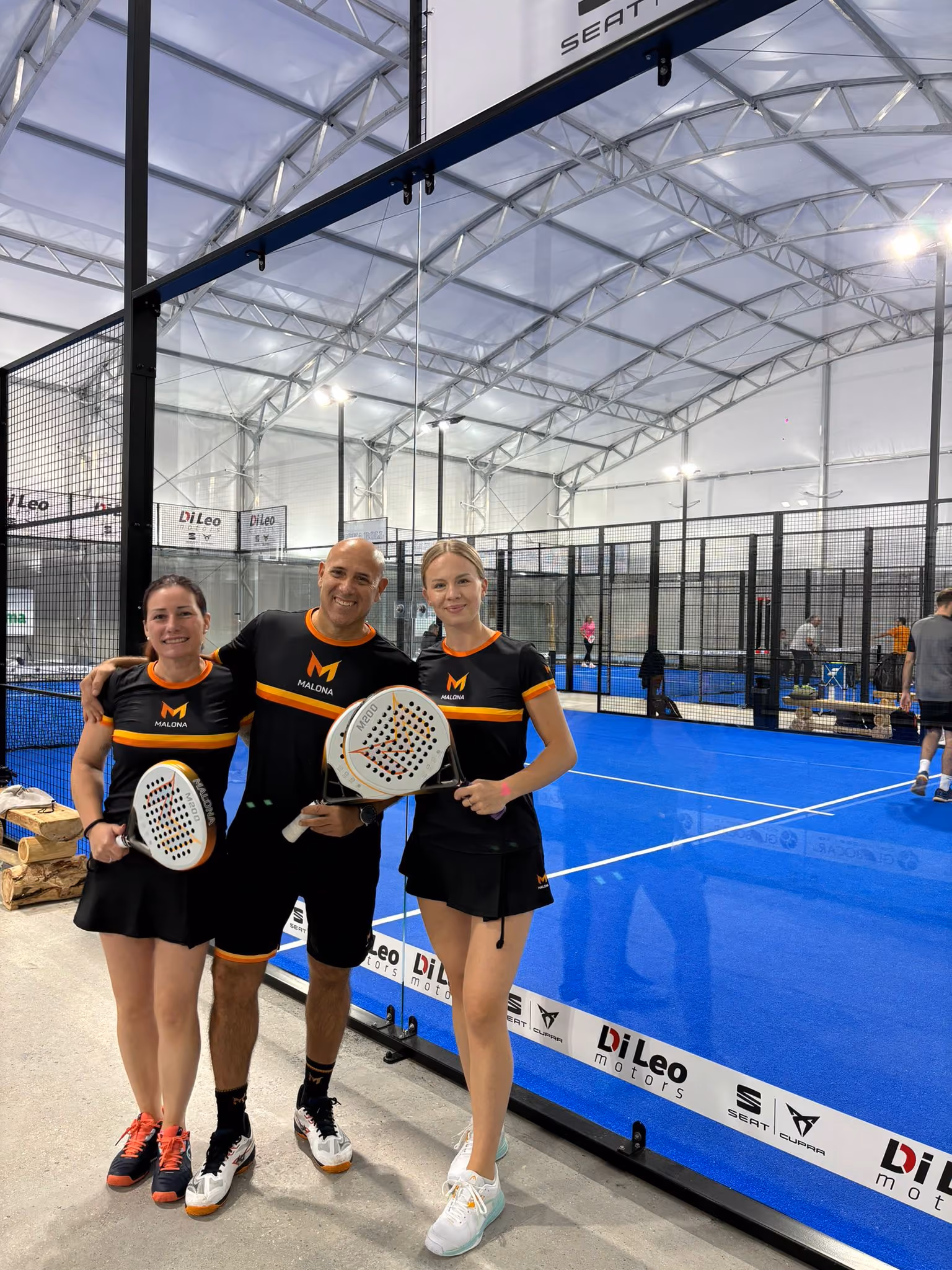 Quattro uomini in piedi su un campo da padel blu con racchette, davanti a una rete.