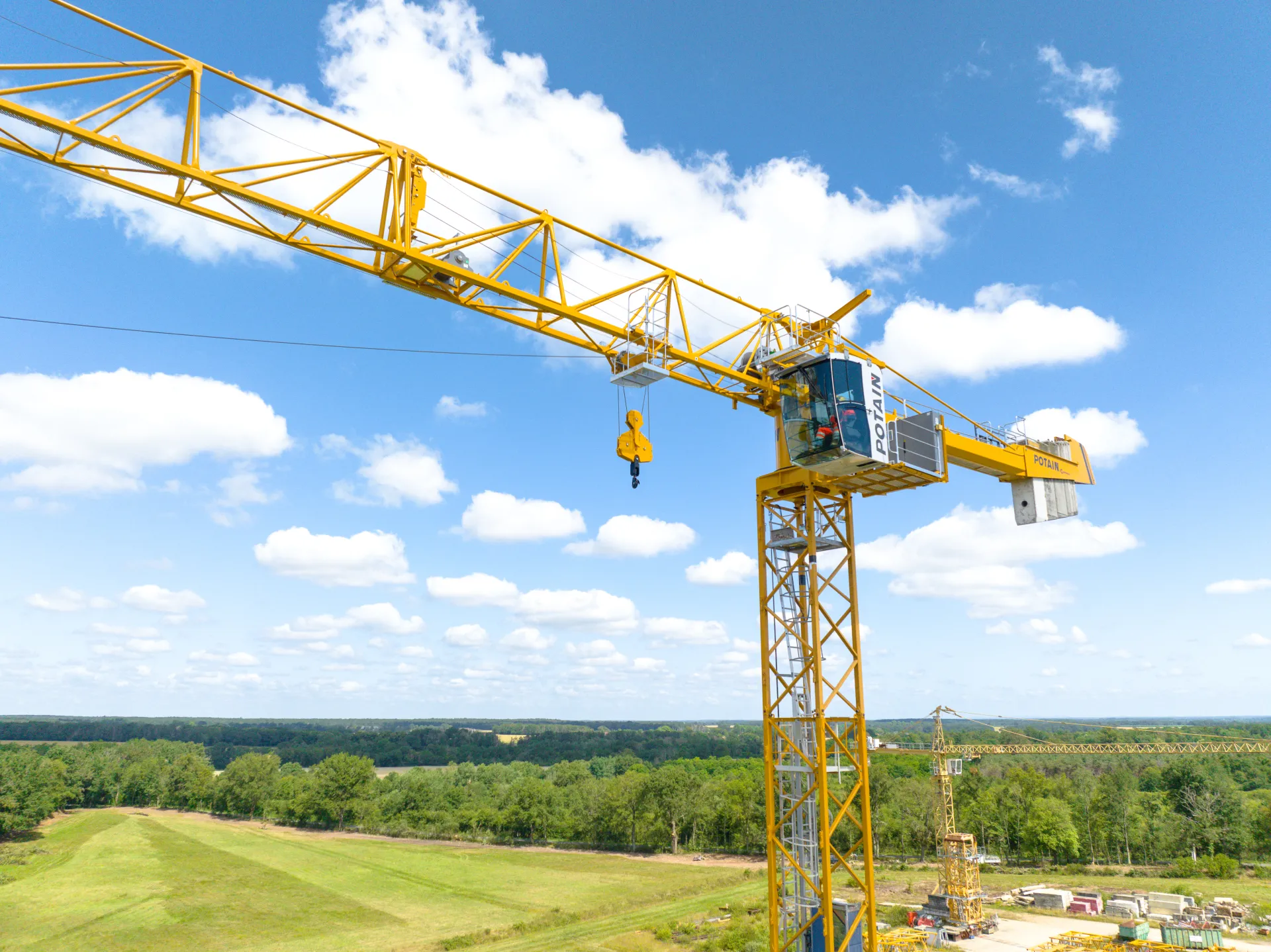Grande grue de construction jaune sur un terrain vert sous un ciel bleu avec des nuages blancs.