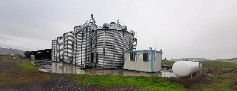 Grands silos en métal et conteneur sur exploitation agricole sous ciel gris.