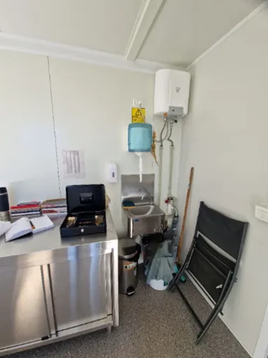 Petite salle avec évier, distributeur de savon, chaise pliable et comptoir en inox.