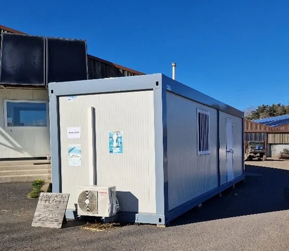 Un conteneur modulaire blanc avec une unité de climatisation extérieure sous un ciel bleu clair.