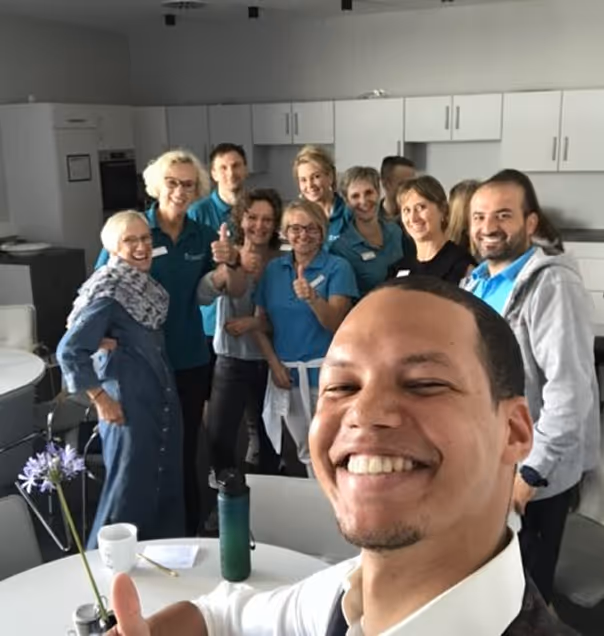 Gruppe von elf Personen in einem Büro, die lächelnd und mit Daumen hoch in die Kamera posieren.
