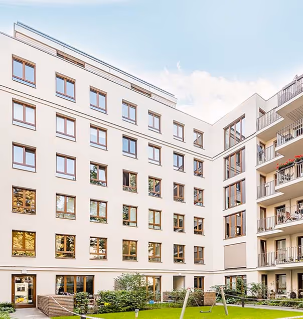 Moderner Wohnblock mit mehreren Fenstern und Balkonen um einen begrünten Innenhof mit einer Schaukel.