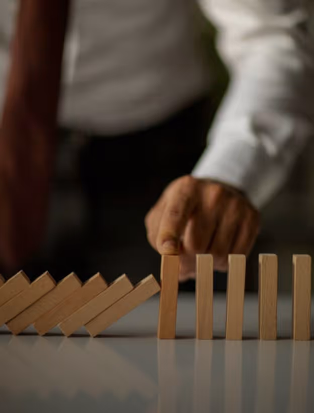 Hand stoppt fallende Holzklötze in einer Domino-Reihe.