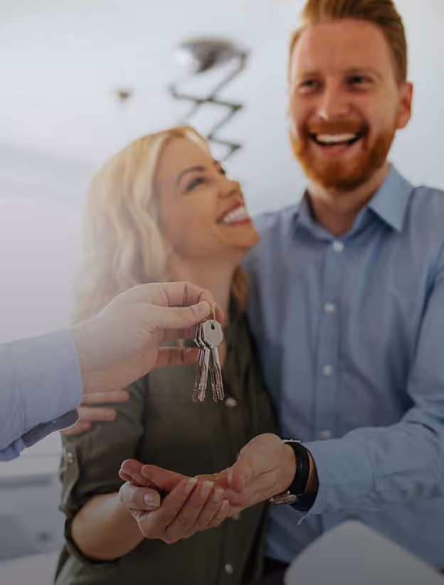 Ein lächelndes Paar erhält Schlüssel von einer dritten Person, Symbol für Immobilienkauf oder Miete.