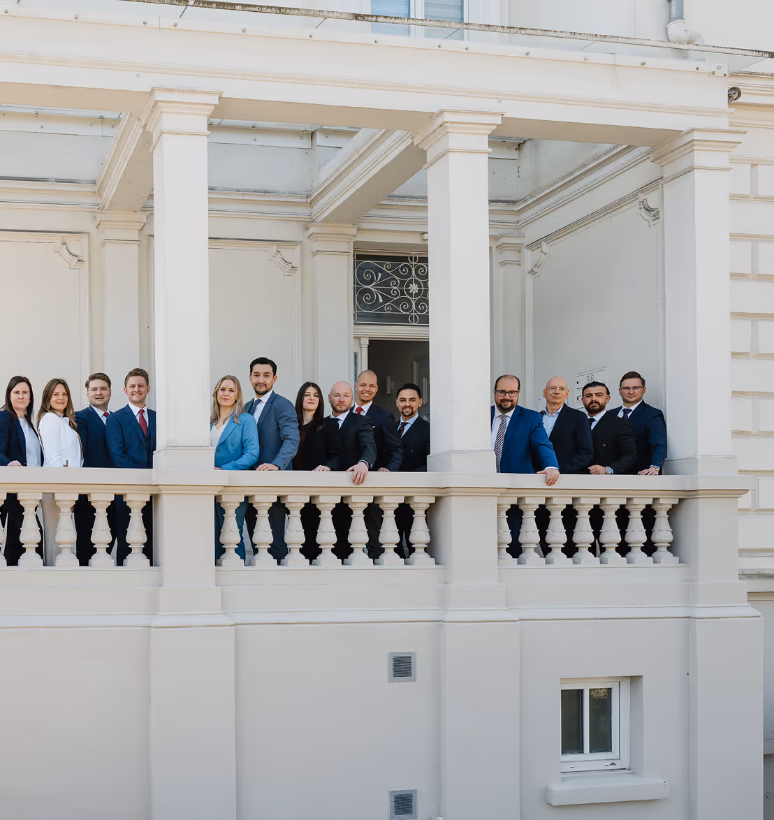 Gruppe von 14 Personen in Geschäftskleidung steht auf einem Balkon eines klassischen Gebäudes.