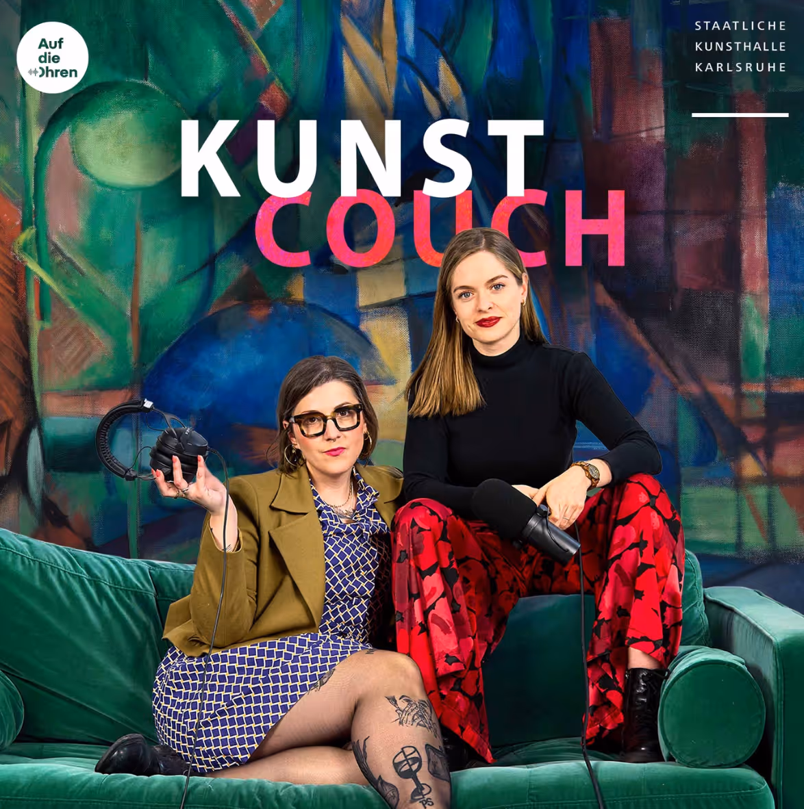 Zwei Frauen sitzen auf grüner Couch vor bunter abstrakter Wand, eine hält Kopfhörer, andere Mikrofon.