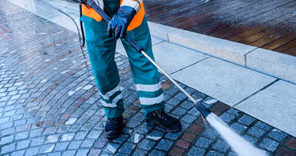 Arbeiterin reinigt mit Hochdruckreiniger nasses Pflaster auf Gehweg.