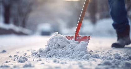 Person schiebt Schnee mit einer roten Schneeschaufel auf einem verschneiten Weg.