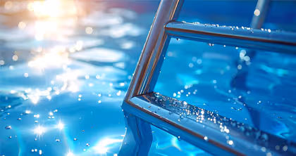 Nahaufnahme einer Poolleiter in klarem blauem Wasser mit Sonnenlichtreflexionen.