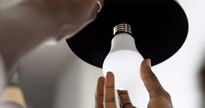 Eine Hand schraubt eine LED-Glühbirne in eine Deckenlampe.