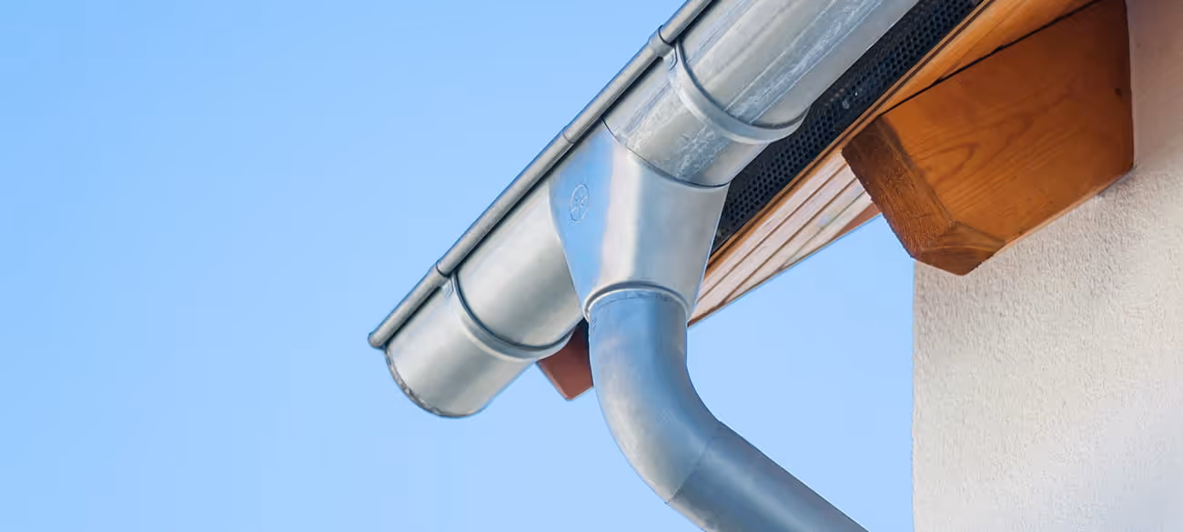 Nahaufnahme eines sauberen Dachrinnensystems aus Metall vor blauem Himmel.