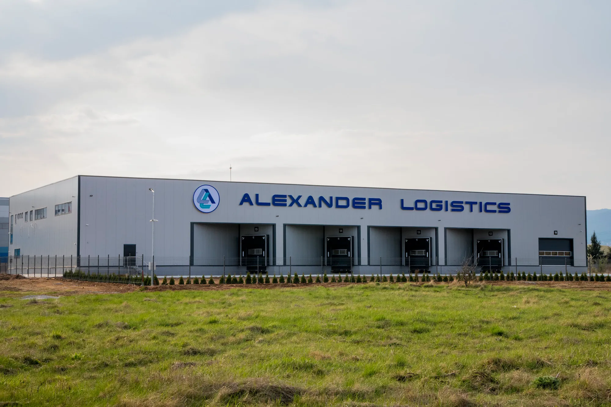Alexander Logistics warehouse with company logo and signage, five loading dock doors, green grass in foreground