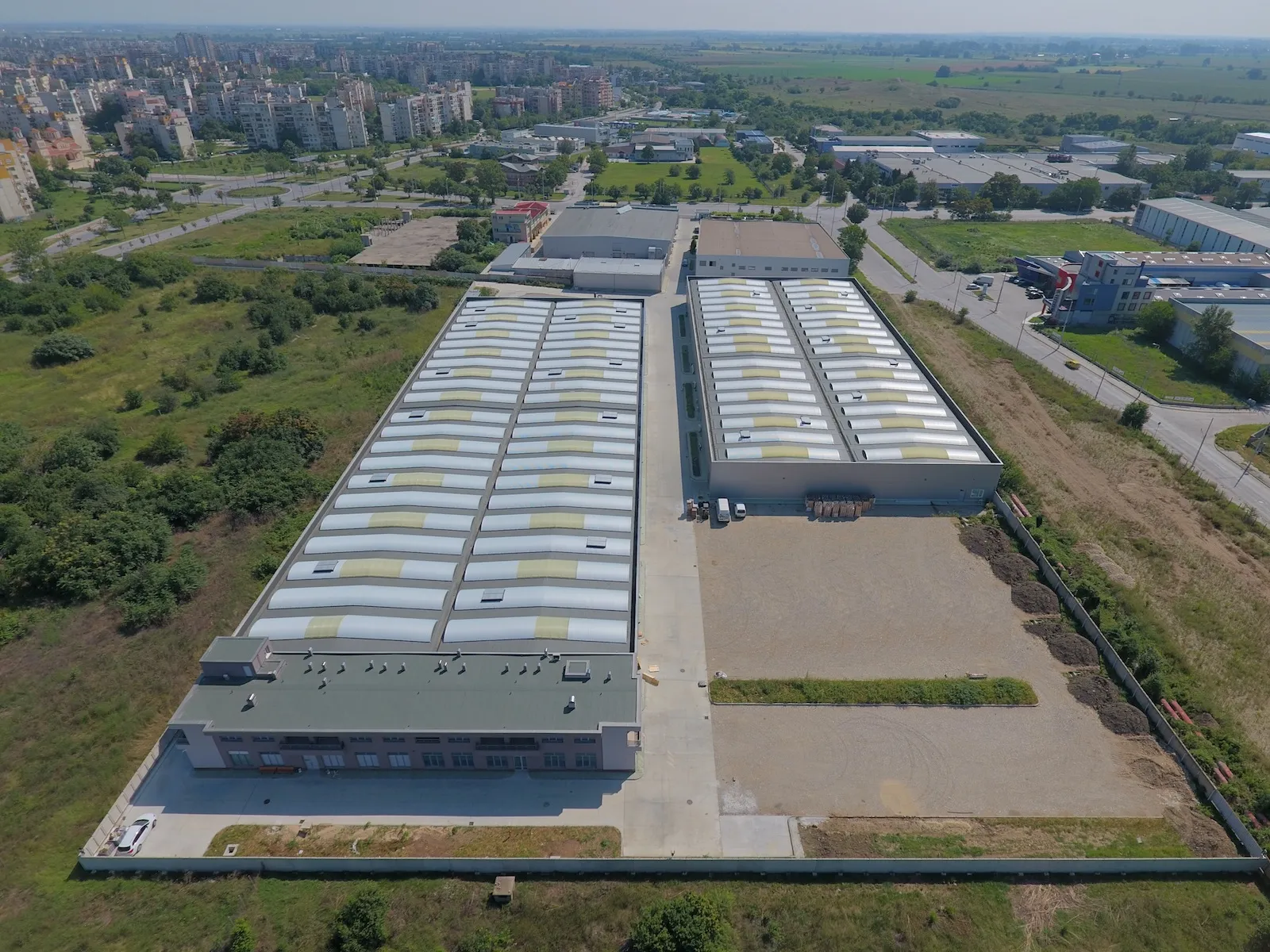 Aerial view of two parallel industrial warehouse buildings with corrugated roofs in an urban industrial area