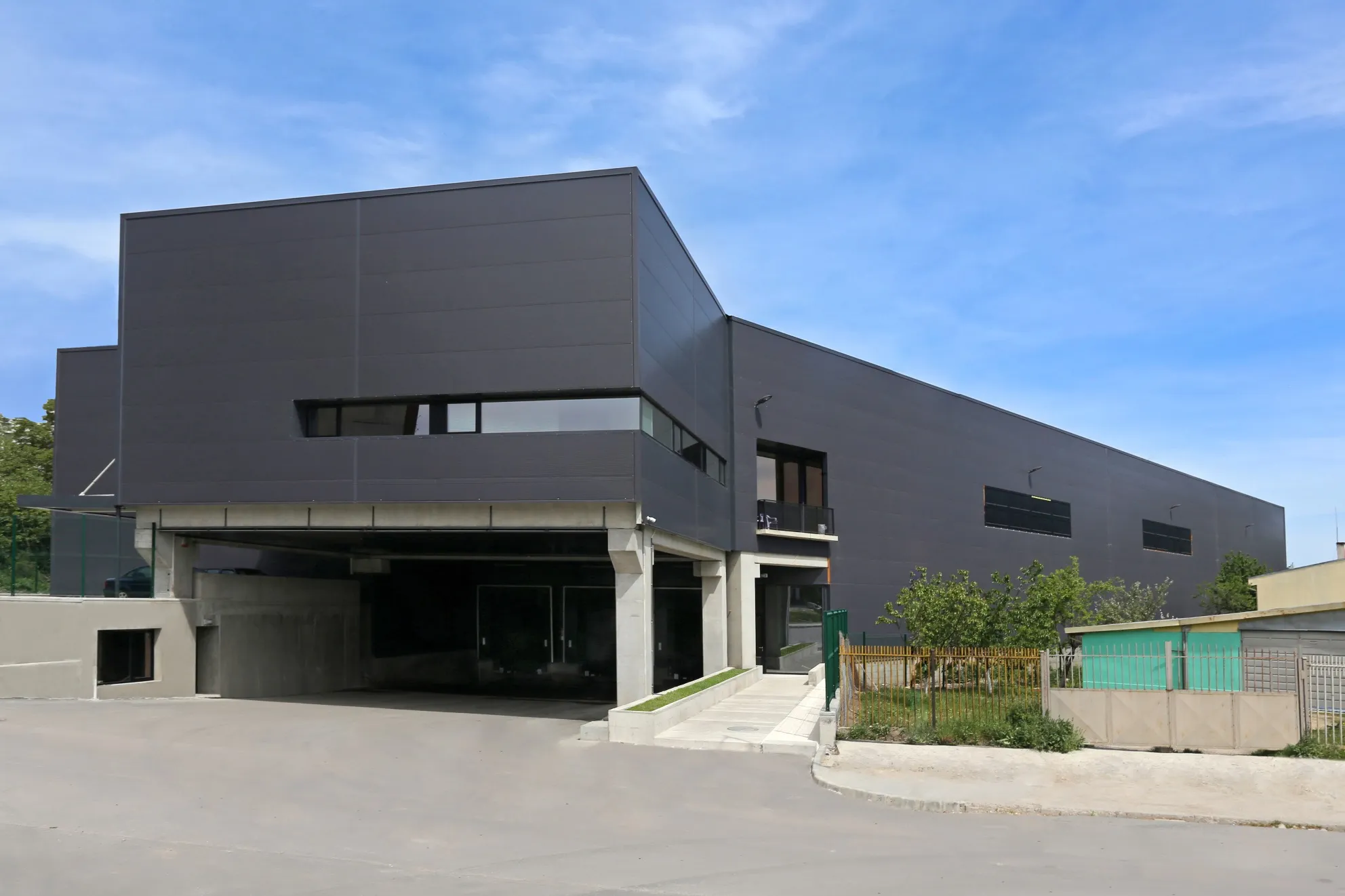 Modern dark grey commercial building with elevated office block, glazed ground floor, and underground parking entrance