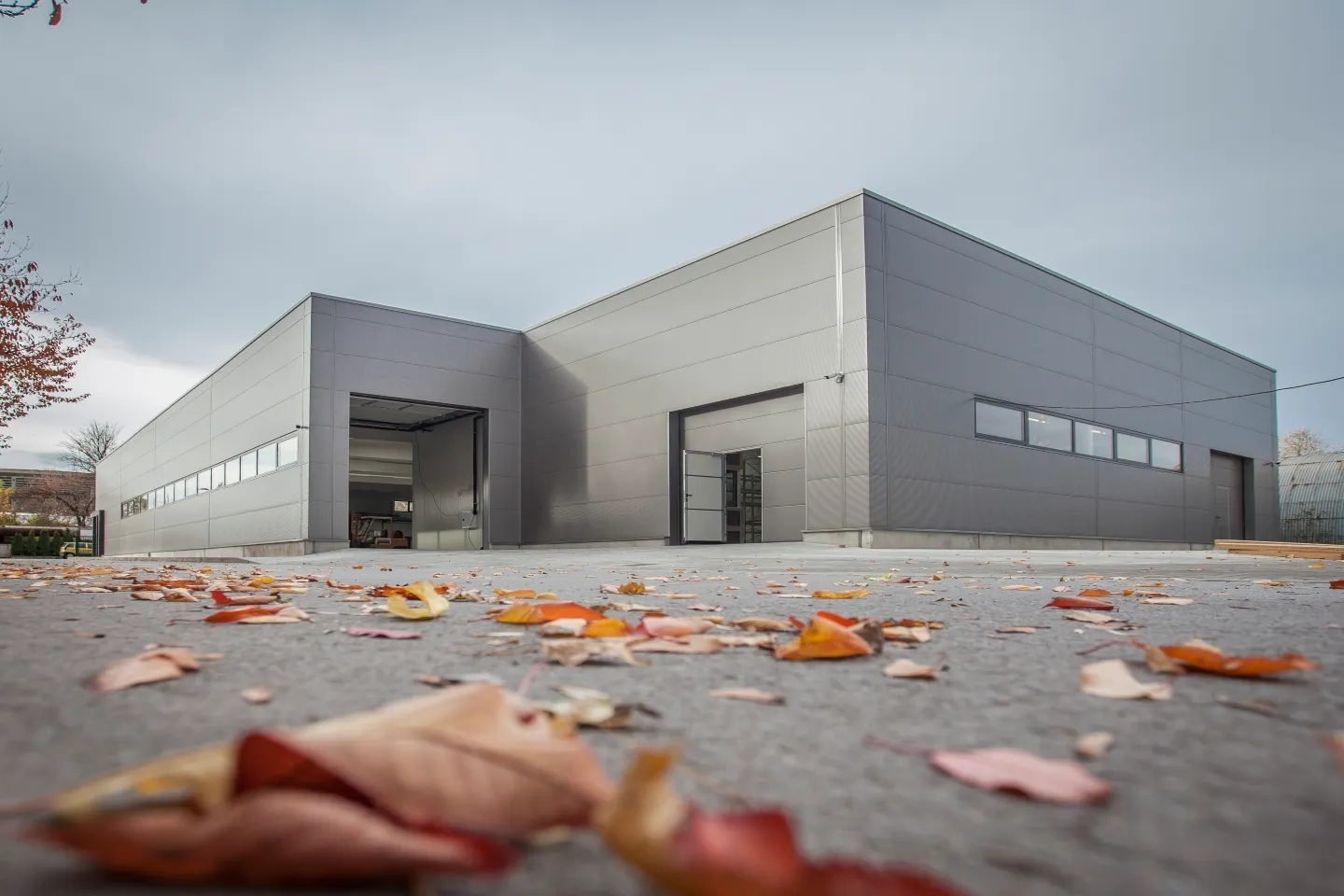 Exterior of a modern grey industrial building with open roller doors and autumn leaves on the ground