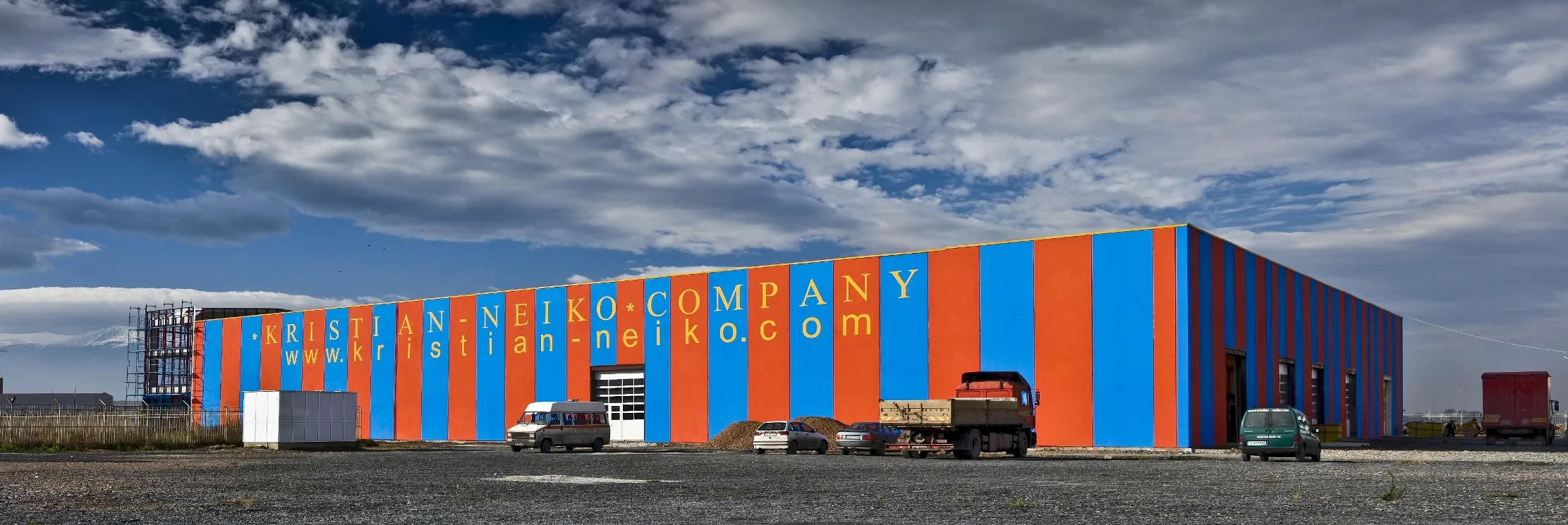 Wide industrial warehouse with bold blue and orange vertical striped facade branded Kristian-Neiko Company