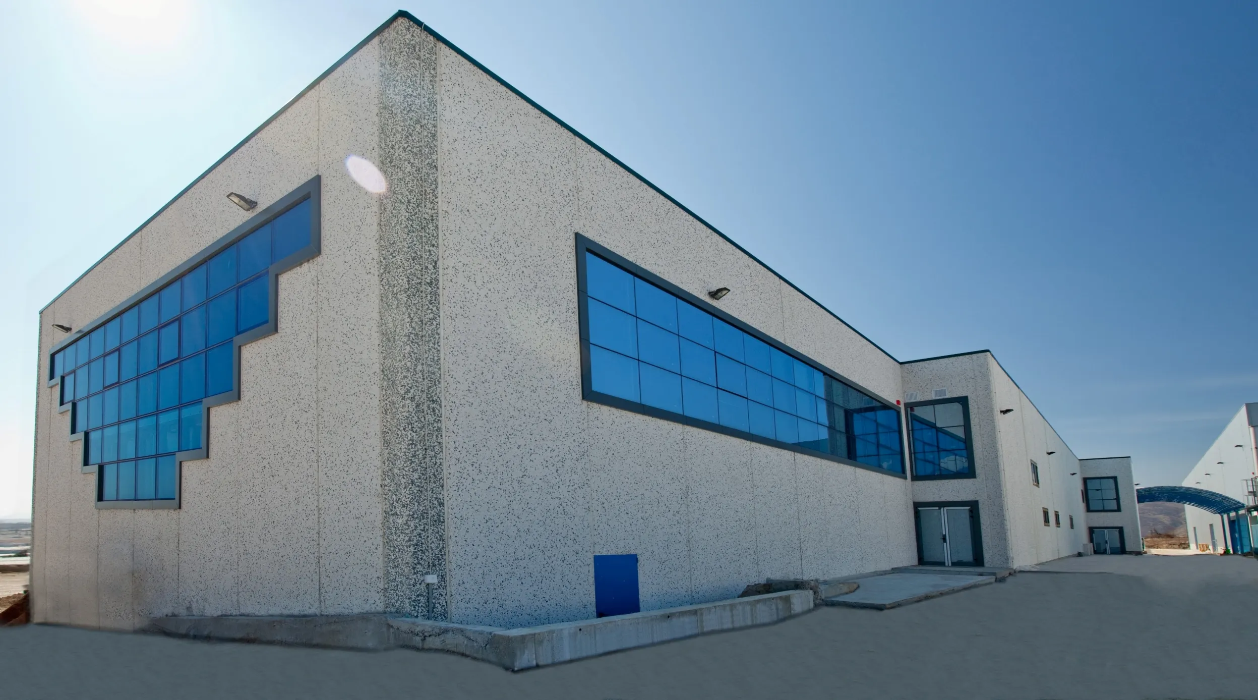 Modern industrial building with speckled grey facade and large blue-tinted curtain glass windows on two facades