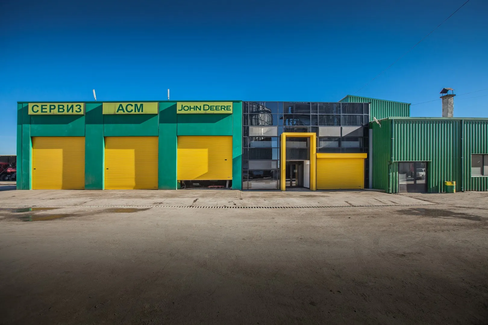 Green and yellow John Deere agricultural service centre with four roller shutter bays and glazed office section