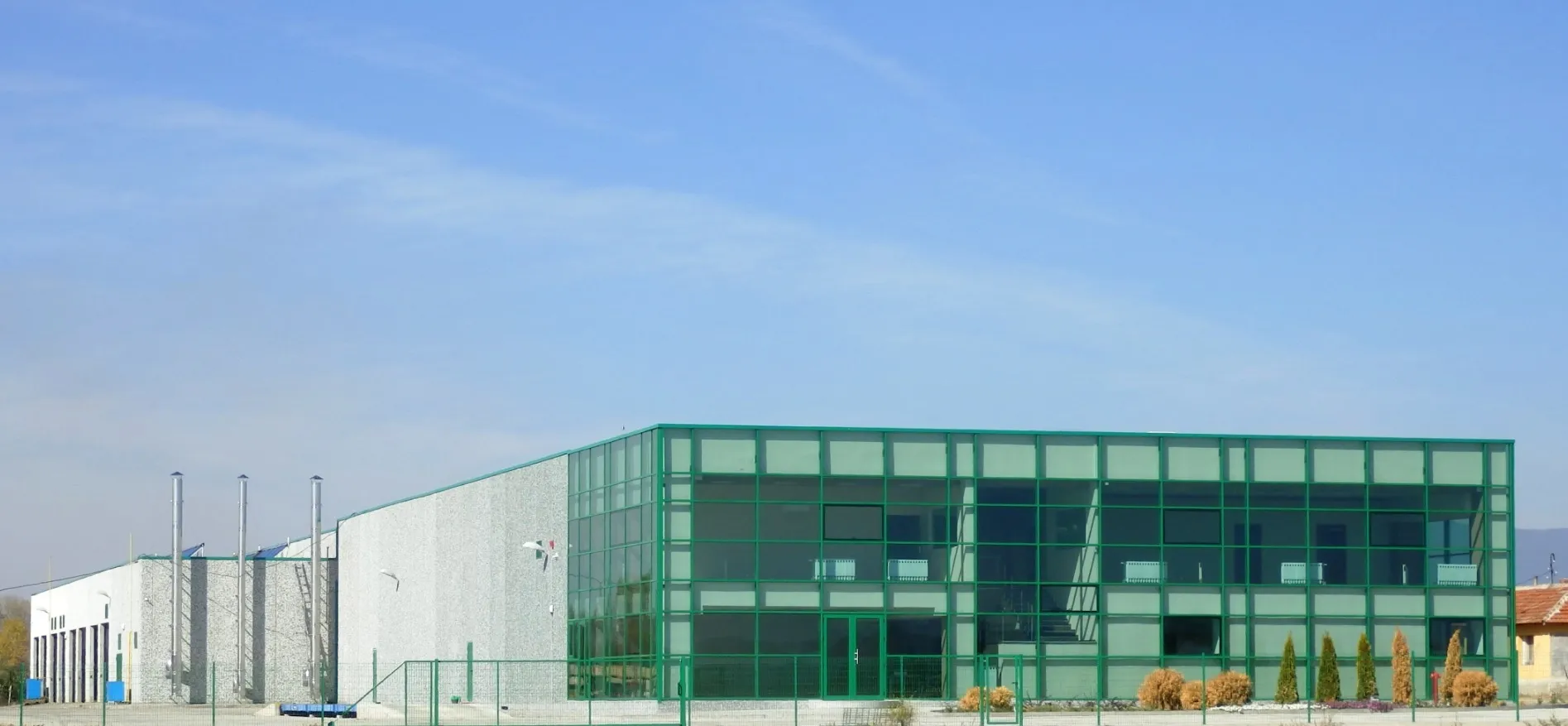 Modern two-storey industrial complex with a green curtain-glass facade and adjacent stone-clad production hall