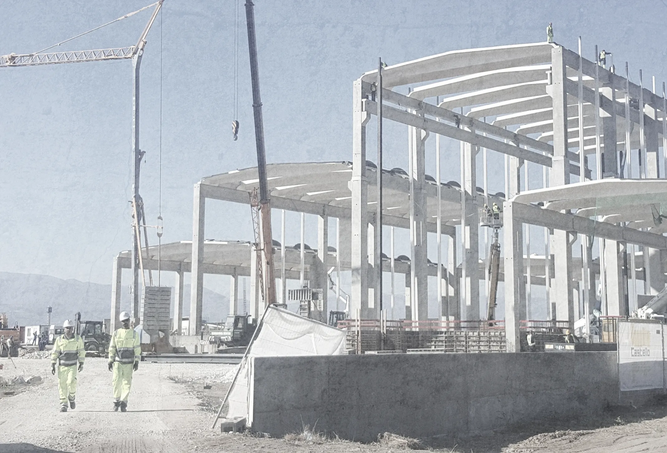 Construction site with concrete frame building, cranes, and workers in safety gear.