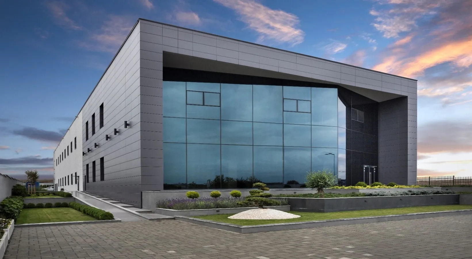 Modern two-story office building with large reflective glass windows and landscaped grounds at dusk.