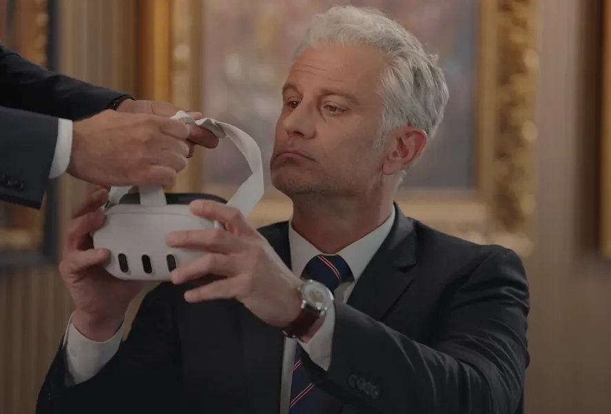 Middle-aged man in a suit holding a virtual reality headset given by another person.