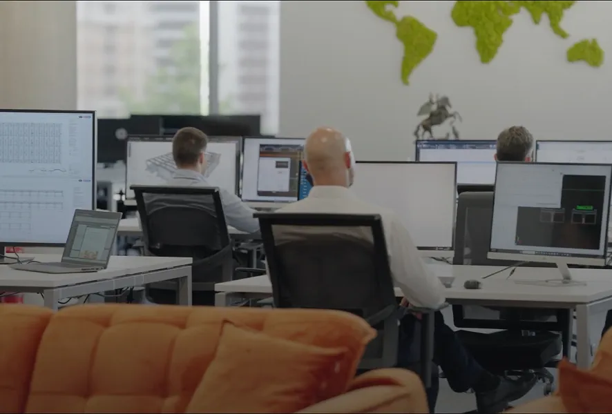 Office space with three people working at desks with computers and an orange couch in the foreground.