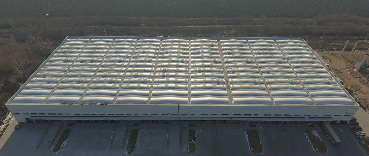 A large industrial building with a white roof featuring protruding skylights and loading docks below.