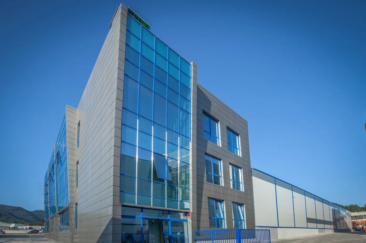 Modern industrial building with glass windows and blue metal siding under clear sky.