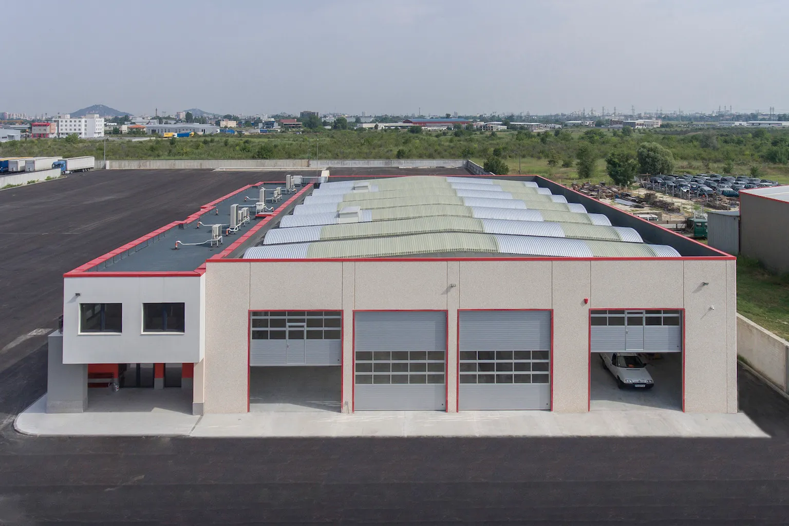 Modern industrial warehouse with four large garage doors, parked car inside one door, and a two-window office.