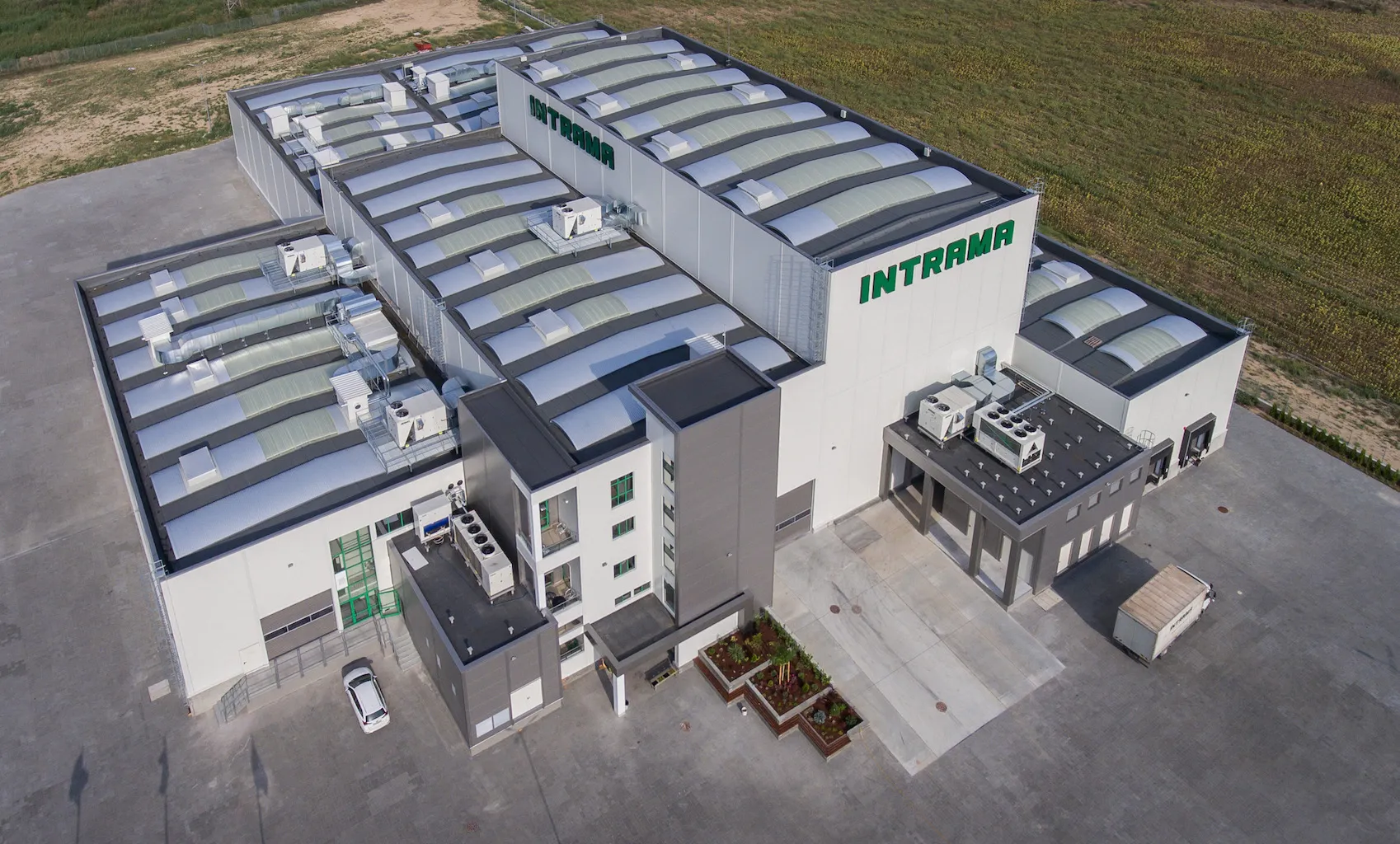 Aerial view of a large industrial building with the word INTRAMA on the facade and surrounding paved area.