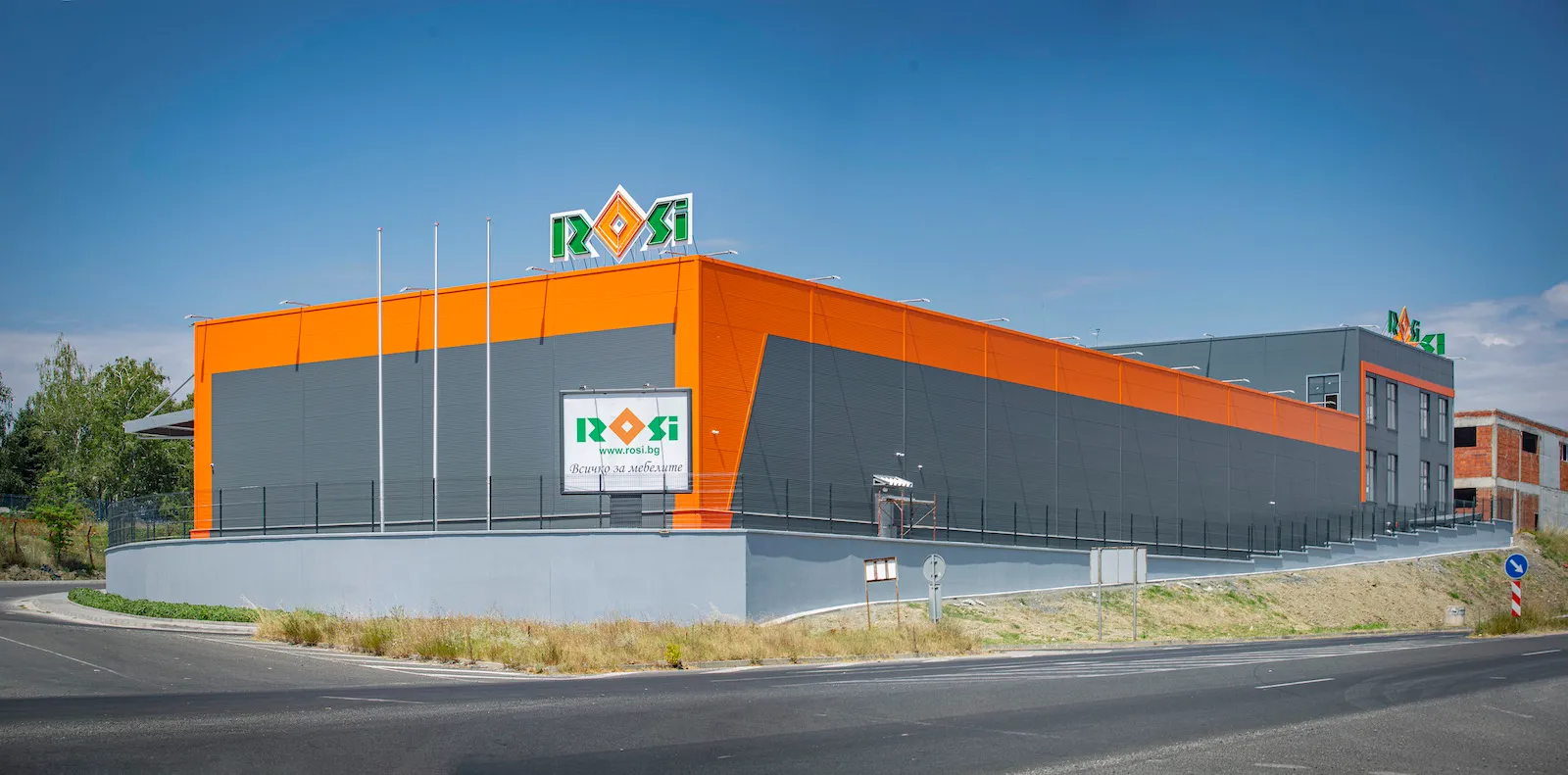 Large modern industrial building in gray and orange with Rosi signage under a clear blue sky.