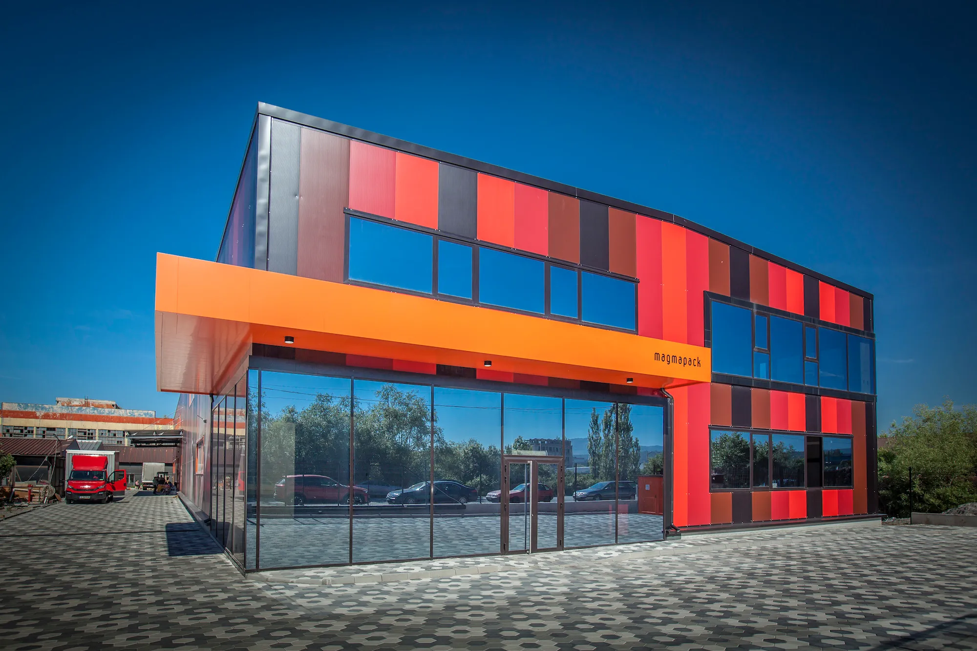 Modern commercial building with red, orange, and black panels and large reflective glass windows.