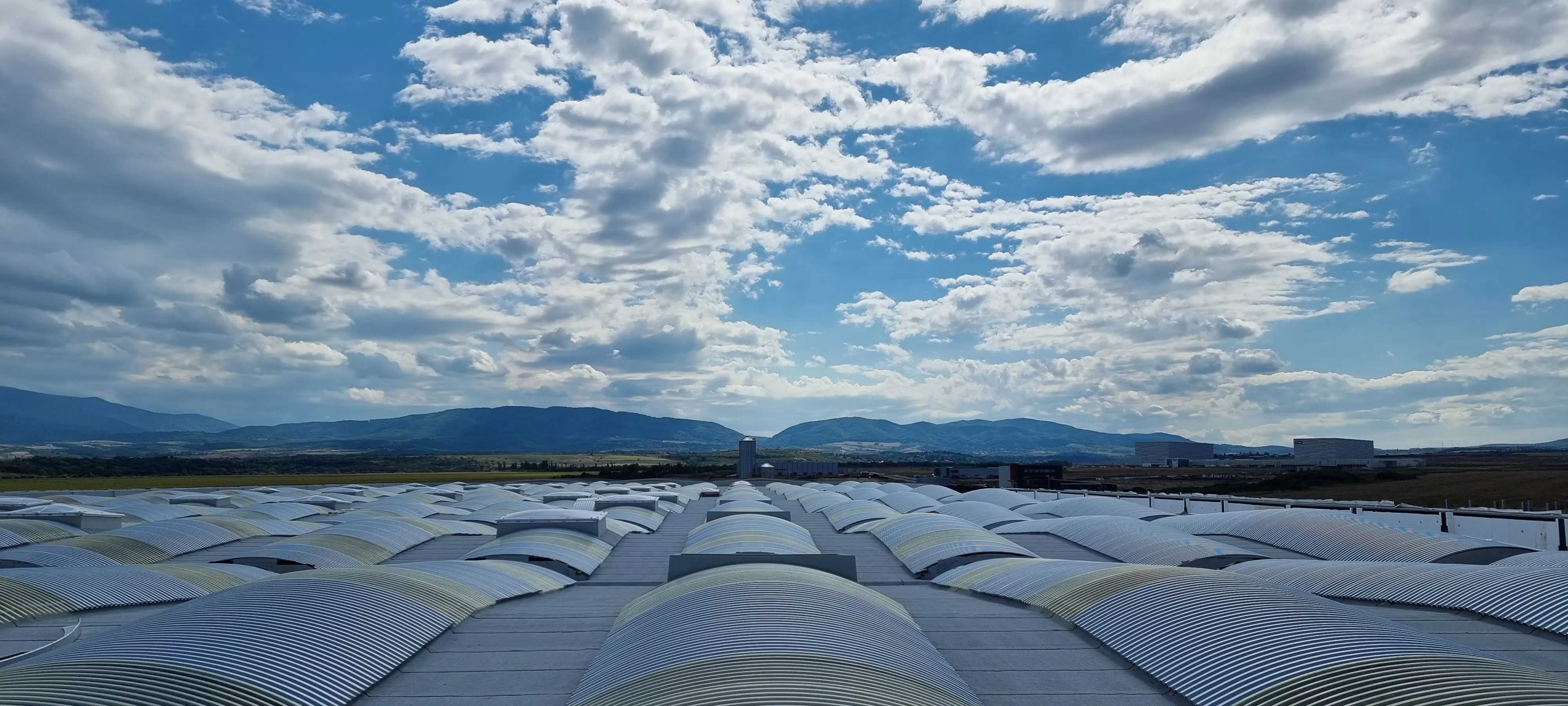 Panoramic view of an industrial rooftop under a cloudy sky with mountains in the distance.