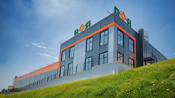 Modern industrial building with a red-framed facade and a company logo on the roof.